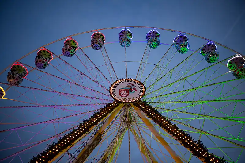 Blick von unten auf ein Riesenrad mit farbig beleuchteten Gondeln vor tiefblauem Abendhimmel.