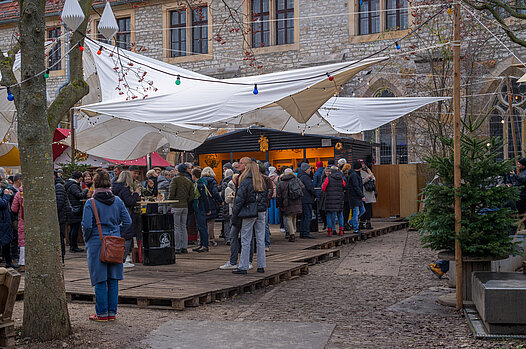 Gedrängter Weihnachtsmarkt im Innenhof: Besucher unter weißen Marktzelten, festliche Lichterketten und bunte Deko am Weg