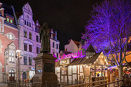 Prächtige Altstadtkulisse am Luthermarkt: Figurensockel mit Laternen, Holzbuden und violett beleuchteter Baum vor Nacht