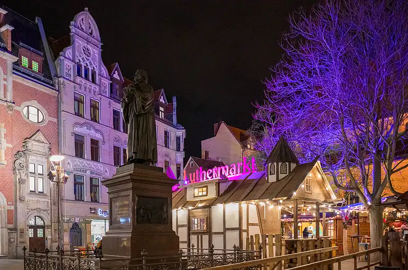Prächtige Altstadtkulisse am Luthermarkt: Figurensockel mit Laternen, Holzbuden und violett beleuchteter Baum vor Nacht
