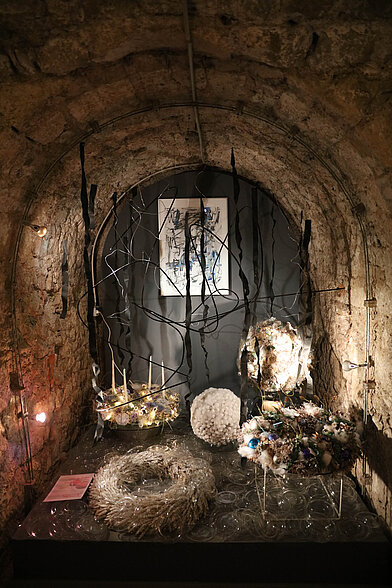 Moderne Floristik mit Adventskranz, Strohring und abstraktem Bild in beleuchteter Steinalcove des Gewölbes.
