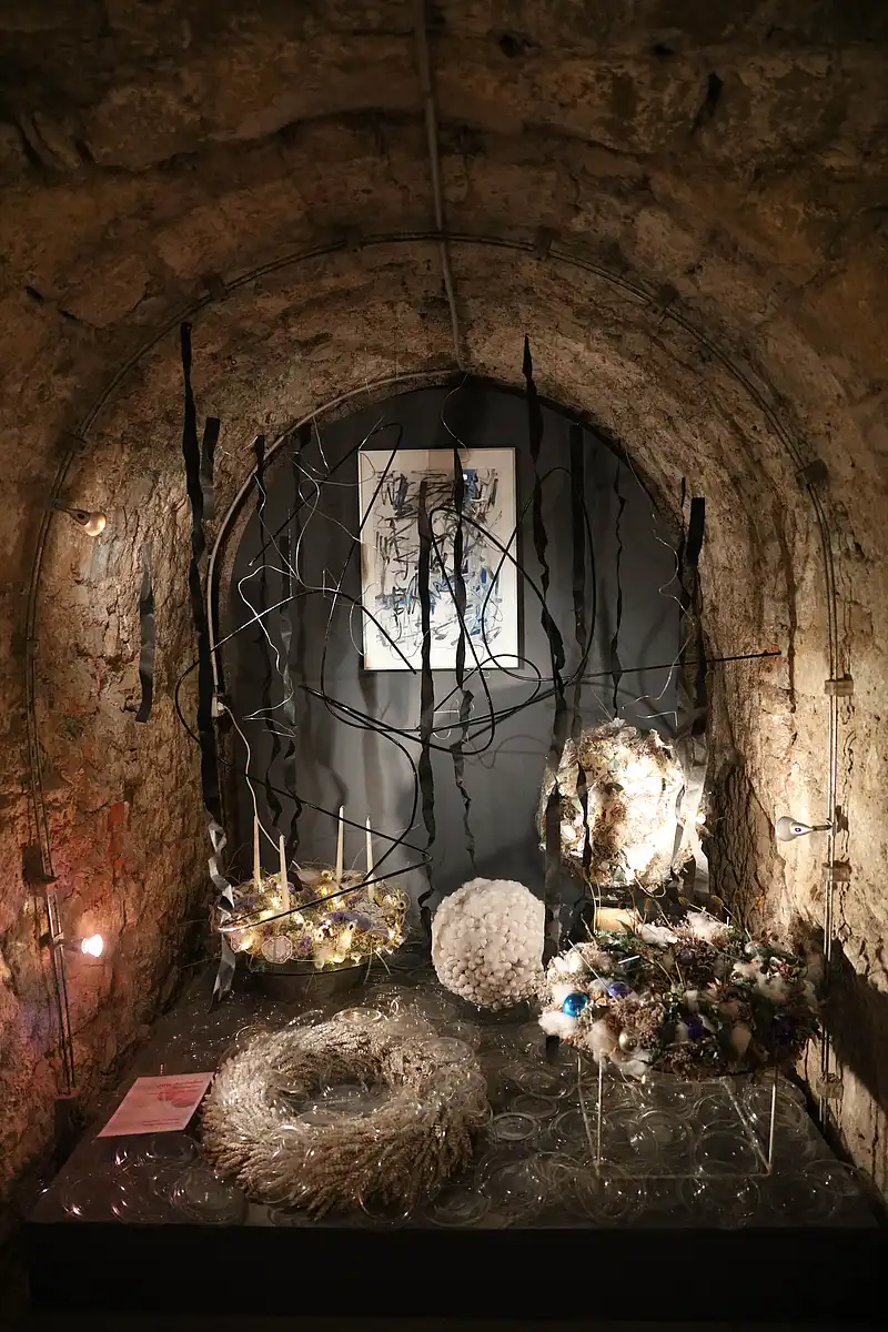 Moderne Floristik mit Adventskranz, Strohring und abstraktem Bild in beleuchteter Steinalcove des Gewölbes.