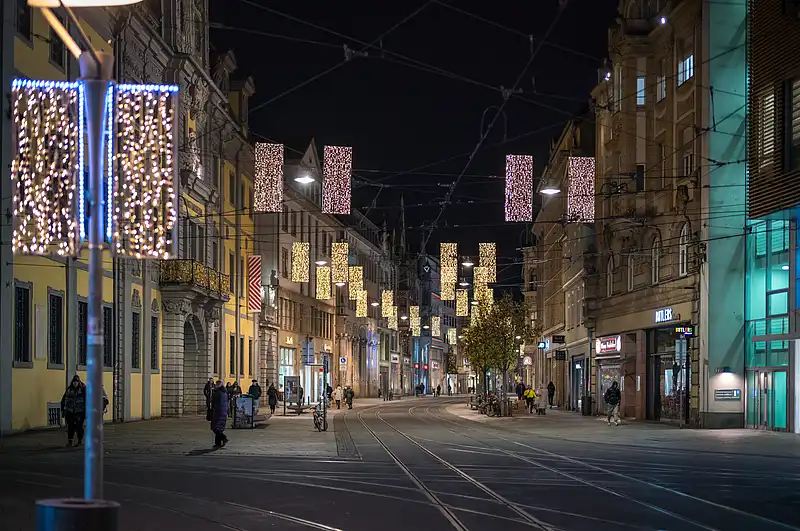Weihnachtlich beleuchteter Anger bei Nacht, Lichterketten über den Gleisen, wenige Passanten auf dem Pflaster.