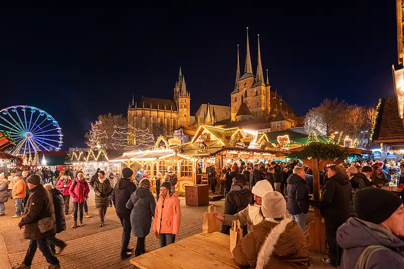 Volle Budengassen am Domplatz, im Hintergrund Domkulisse und Riesenrad, warmes Licht und viele Menschen.