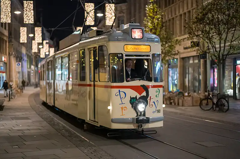 Nahaufnahme der Straßenbahn am Weihnachtsmarkt: Lichter im Hintergrund und Fassaden links und rechts.