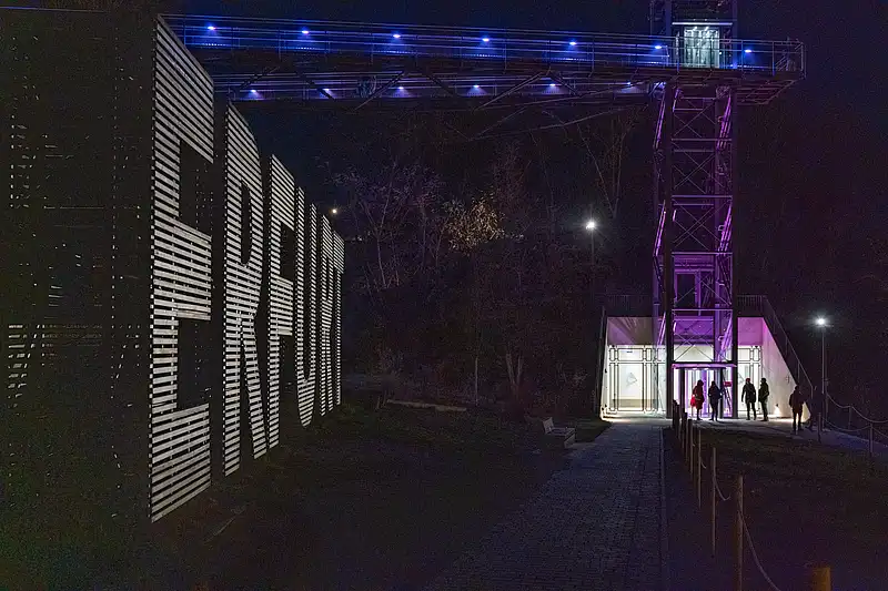 Weihnachtsmarkt-Eingang bei Nacht mit blau-violetten Lichtbögen, Menschen spazieren über den beleuchteten Weg