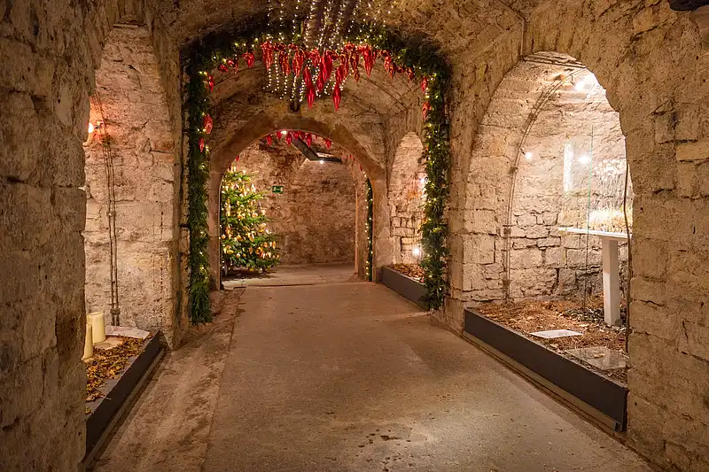 Tannengirlande mit roten Zapfenanhängern und Lichterketten schmücken Torbogen zum Weihnachtsbaum im Gewölbe.