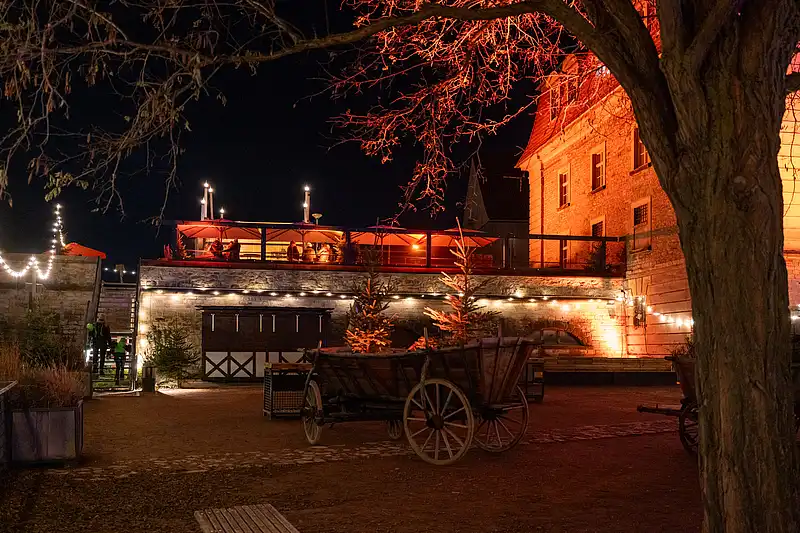 Weihnachtsmarkt bei Nacht: beleuchtete Pferdekutsche und hölzerner Aufbau vor warm angestrahlter Steinfassade