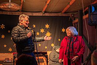 Auf weihnachtlich dekorierter Bühne präsentiert Pfarrer Christoph Knoll die Sängerin Gerda Gabriel vor Sternen-Dekohintergrund.