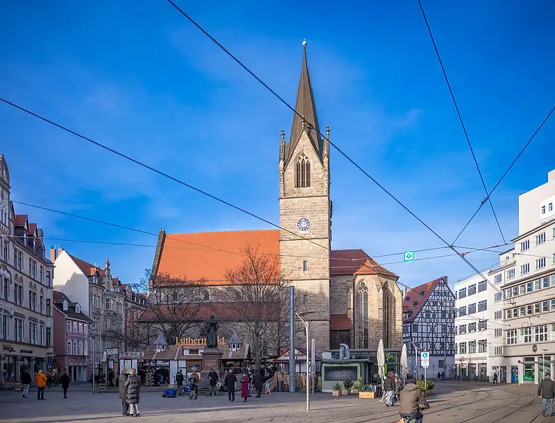 Blick auf den Luthermarkt mit Kirchturm, festlich geschmückten Buden, Menschenmenge und warmem Licht
