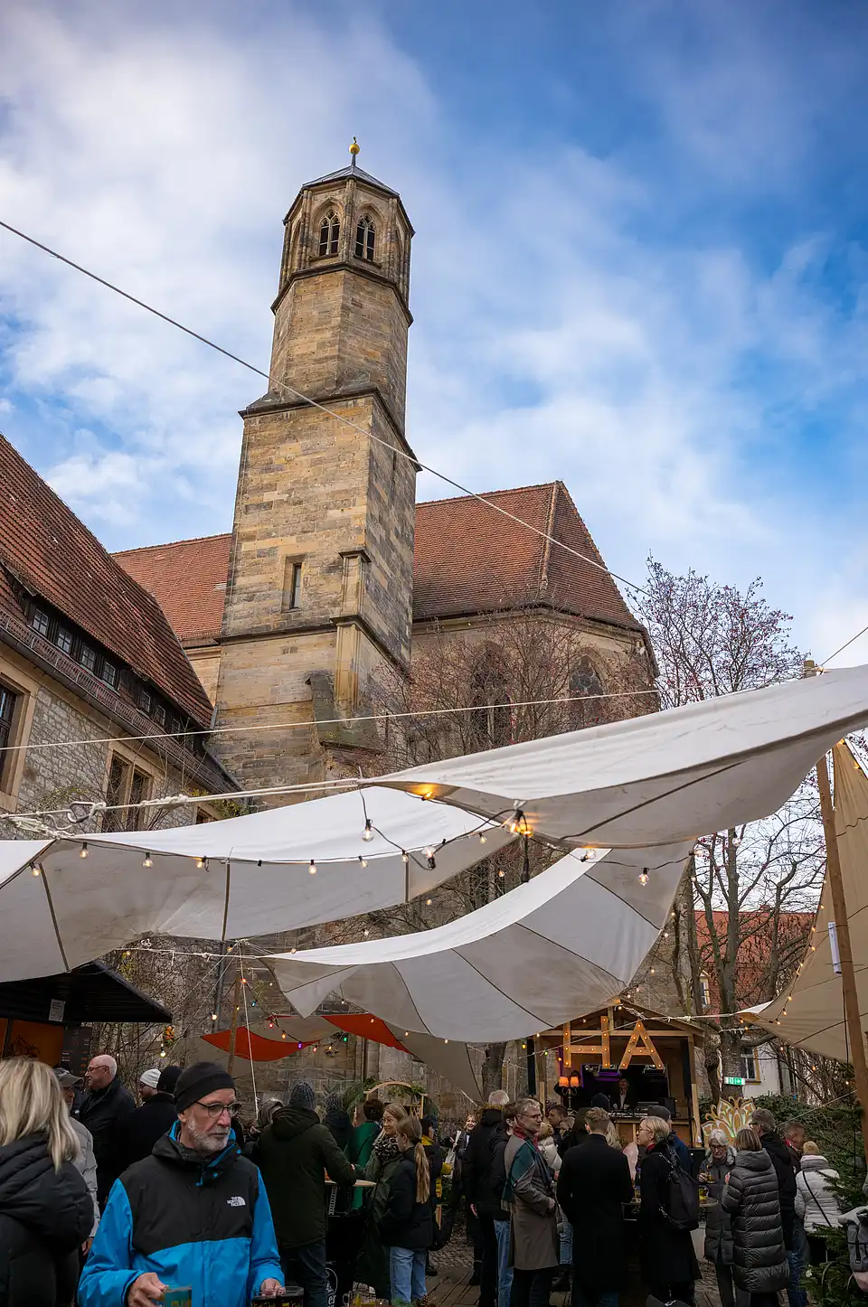 Weihnachtsmarkt tagsüber: Blick auf den hohen Kirchturm über vollen Marktständen und warmen Zeltbeleuchtungen