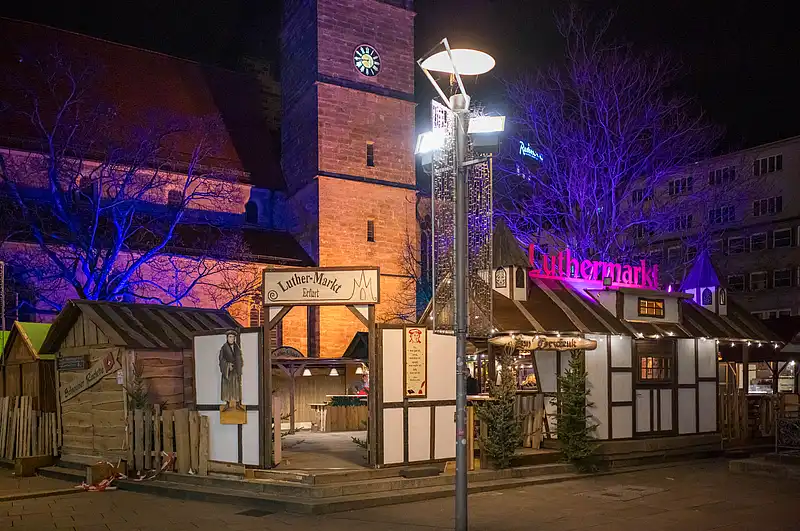 Eingang zum Luthermarkt mit beleuchteter Säule, Wegweisern und Fachwerkhäusern im Nachtlicht