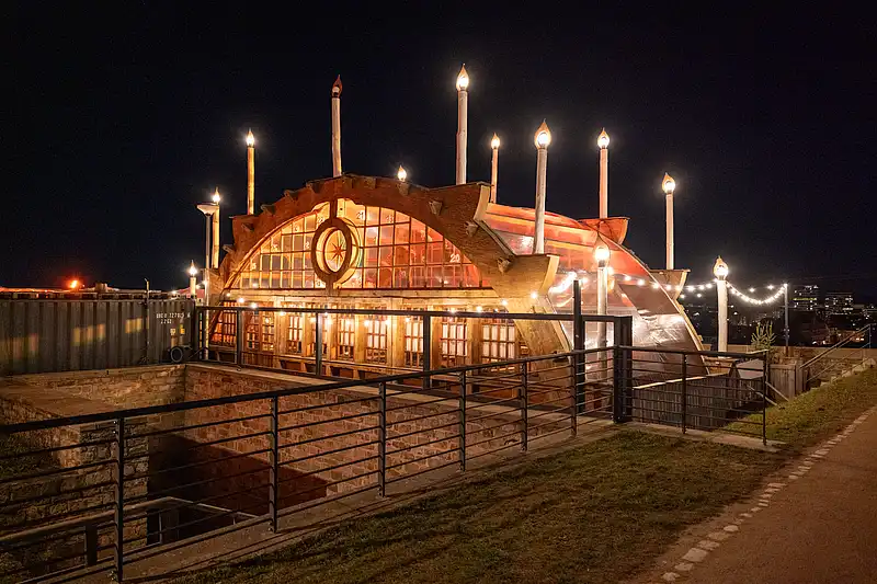 Festlich beleuchteter Pavillon mit Glasfront und hohen Kerzenstelen, davor Geländer und Winterweg in der Nacht.