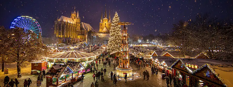 Überblick bei Schneetreiben: Karussell mit Kegeldach, Christbaum, Pyramide und Dom im Hintergrund